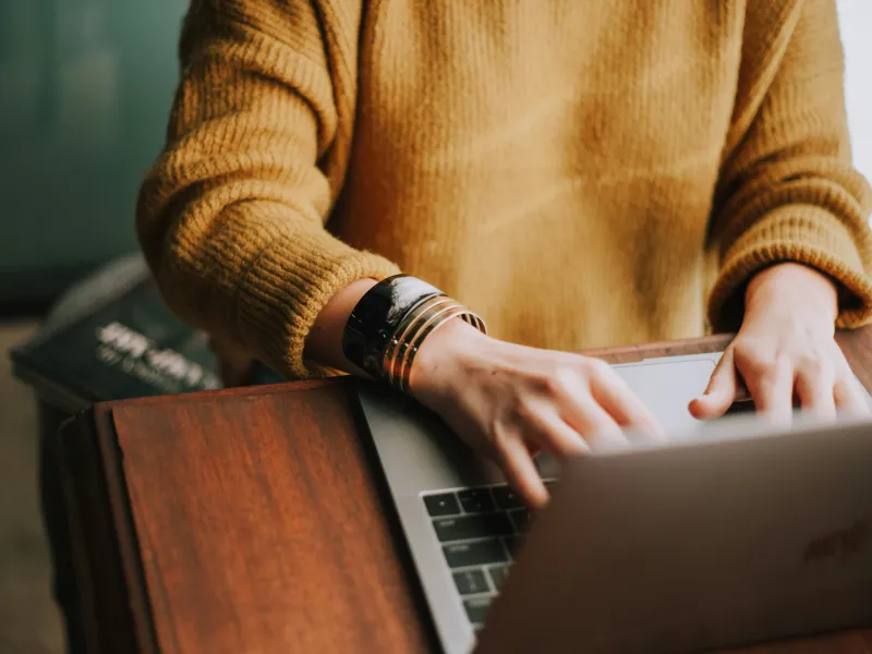 Person wearing a mustard-yellow sweater uses a laptop computer.